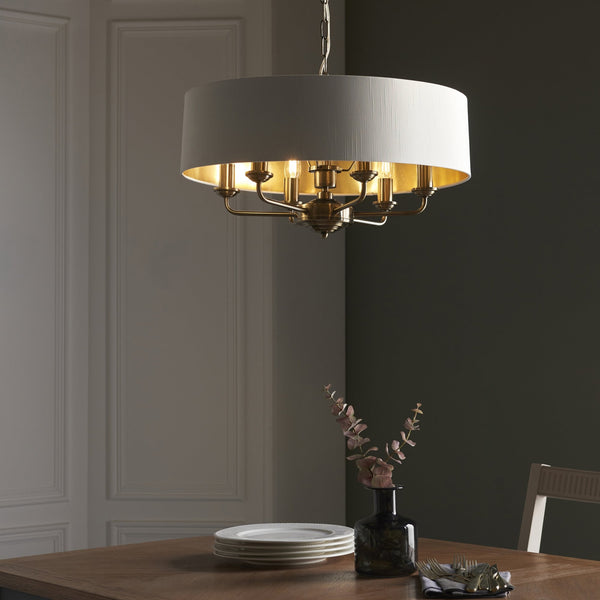 Endon Highclere 6-Light Pendant Drum Light Antique Brass – A refined pendant light featuring a vintage white fabric shade, gold metallic lining, and antique brass-plated metalwork. Height-adjustable and dimmable, this elegant fixture is perfect for dining rooms, living spaces, and bedrooms, offering a warm, sophisticated glow.