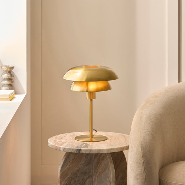 Satin brass layered-shade table lamp glowing on a marble side table