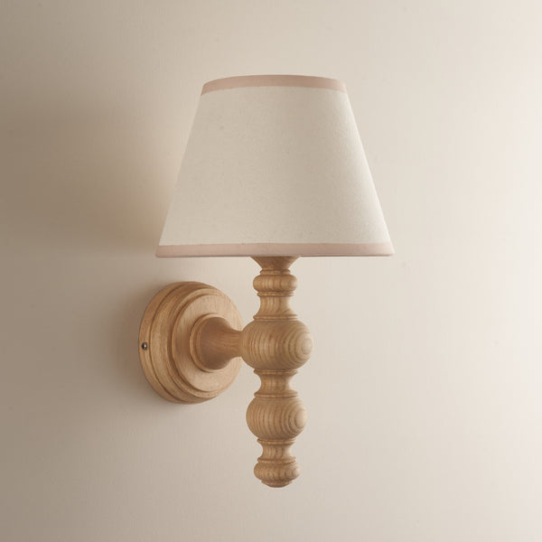 Bibury Wall Light in natural ash & vintage white lit up in a room setting