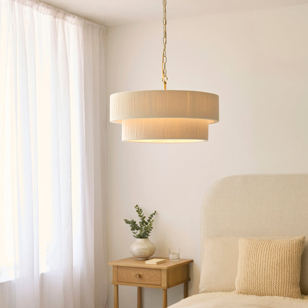 Noah 5 Light Tiered Pendant in brushed brass and cream cotton hanging in a living room