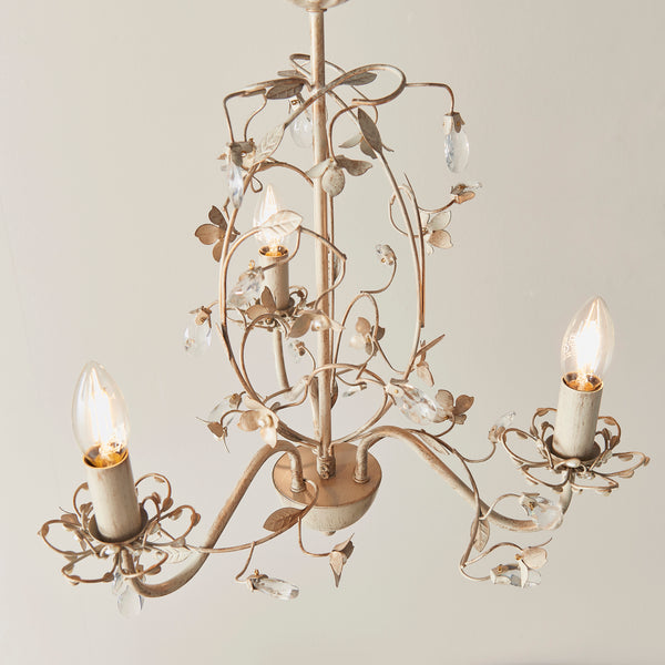 Lullaby 3 Light Chandelier in cream and brushed gold hanging in a bedroom