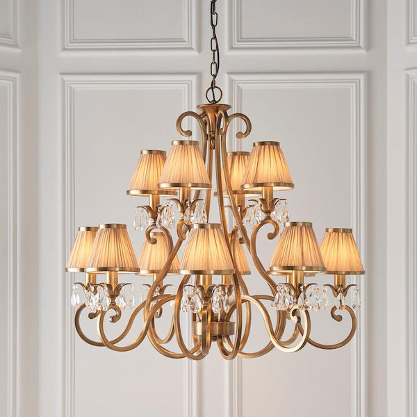 Interiors 1900 Oksana 12-Light Chandelier in Antique Brass with Beige Shades – A classic chandelier featuring antique brass detailing, faceted crystal accents, and beige fabric shades. Adjustable height (78cm-177cm), dimmable compatibility, and uses 12 x E14 bulbs (not included).