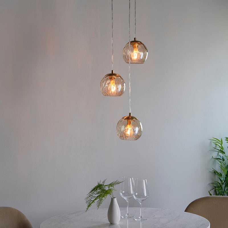 Dimple 3 Light Pendant in satin brass hanging in a dining room