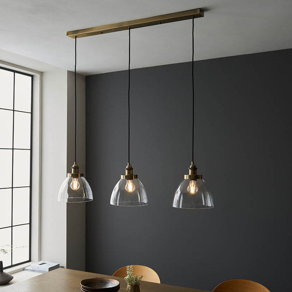 Hansen 3 Light Linear Pendant in antique brass hanging in a kitchen