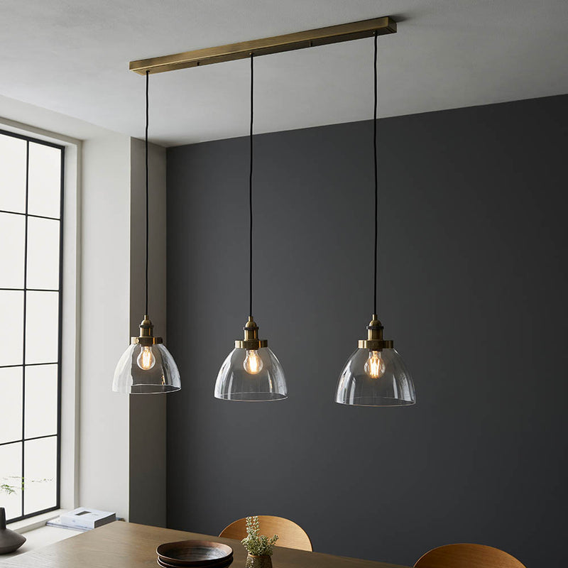 Hansen 3 Light Linear Pendant in antique brass hanging in a kitchen