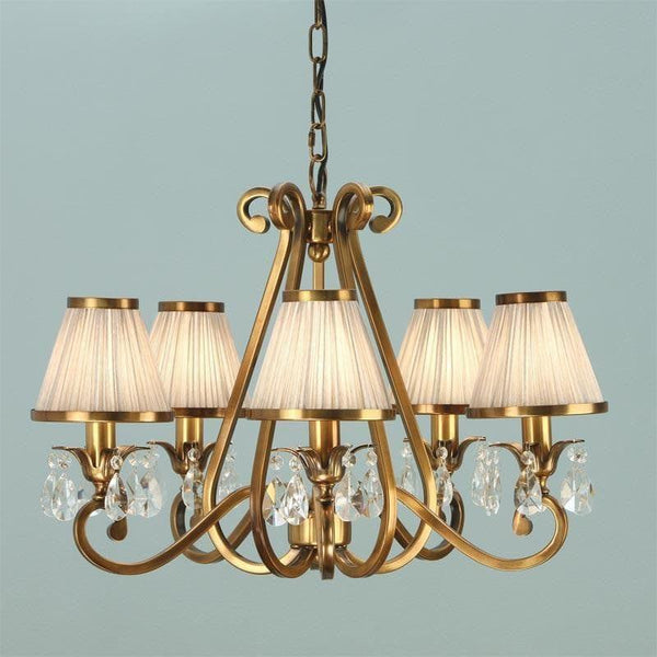 Interiors 1900 Oksana 5-Light Chandelier in Antique Brass & Beige – A traditional chandelier featuring an antique brass finish, faceted crystal details, and five beige fabric shades. Designed for warm, diffused lighting with an adjustable height (59cm-149cm) and dimmable compatibility. Uses 5 x E14 bulbs (not included).