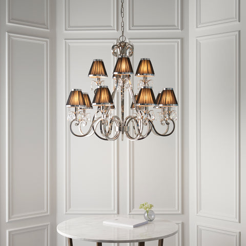 This Oksana 12-light candle chandelier is from our Oksana nickel range by Interiors 1900. The Oskana Nickel 12-light pendant is an impressive candle chandelier fitting. Finished in polished nickel plate. Suitable for hallways, living rooms, and dining rooms.  Features faceted lead crystal droplets and black pleated shades. Matching items are available on request.   This Oksana 12-light nickel-plated pendant is dimmable and suitable for use with LED bulbs. Supplied complete with fixing accessories. 