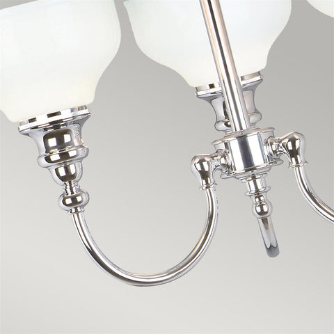 The Elstead Cheadle bathroom 3 light chandeliers in polished chrome finish and rated IP44 boasting traditional period style and opal white glass shades. Featuring a circular ceiling mount and rod suspension, with three curved arms and upward-facing opal white glass bowl shades.