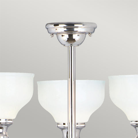 The Elstead Cheadle bathroom 3 light chandeliers in polished chrome finish and rated IP44 boasting traditional period style and opal white glass shades. Featuring a circular ceiling mount and rod suspension, with three curved arms and upward-facing opal white glass bowl shades.